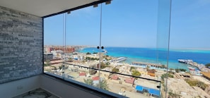 A room with a large window overlooking a coastal cityscape with buildings, a marina, and the sea. - Spacious Rooftop Apartment With Stunning Sea Views in Hurghada (Hurghada)