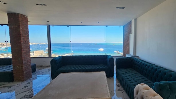 Ein modernes Wohnzimmer mit einem großen Fenster, das Blick auf das Meer und entfernte Gebäude bietet.