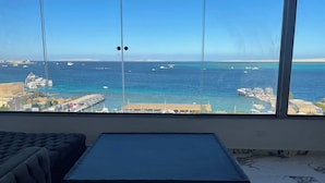 Ein Zimmer mit einem großen Fenster, das Meer und Boote zeigt. Im Vordergrund steht ein dunkelgraues Sofa und ein kleiner Tisch.
