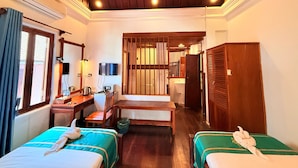 Habitación de hotel con dos camas individuales, un escritorio con silla, televisión y baño visible a través de un umbral.