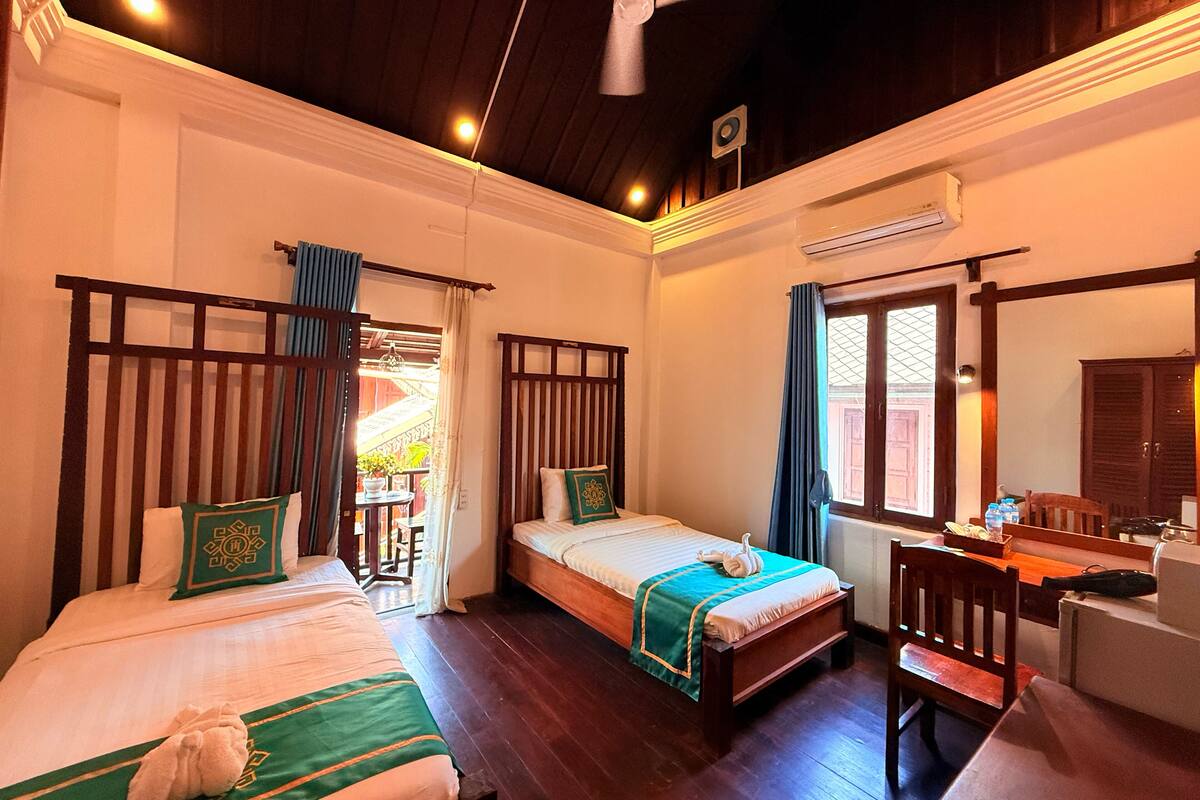 A hotel room with two beds, a ceiling fan, a desk with a chair, and a window with curtains.