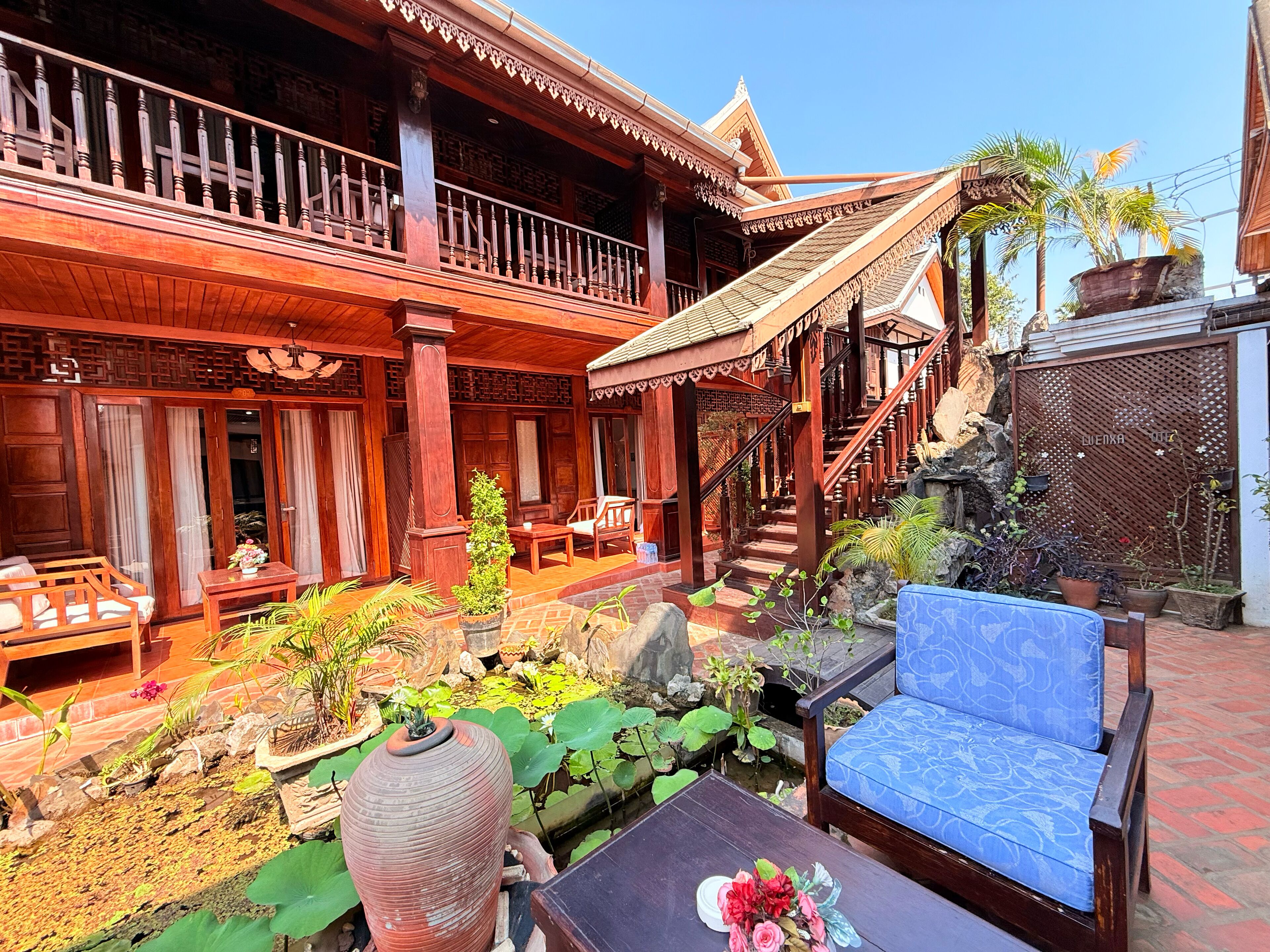 A traditional wooden building with a balcony, outdoor seating, and a small pond with plants.