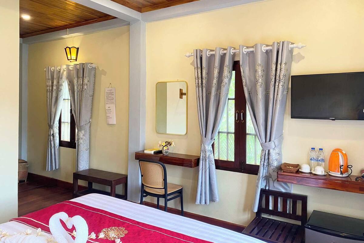 A hotel room with a bed, desk, chair, TV, and a window with curtains.