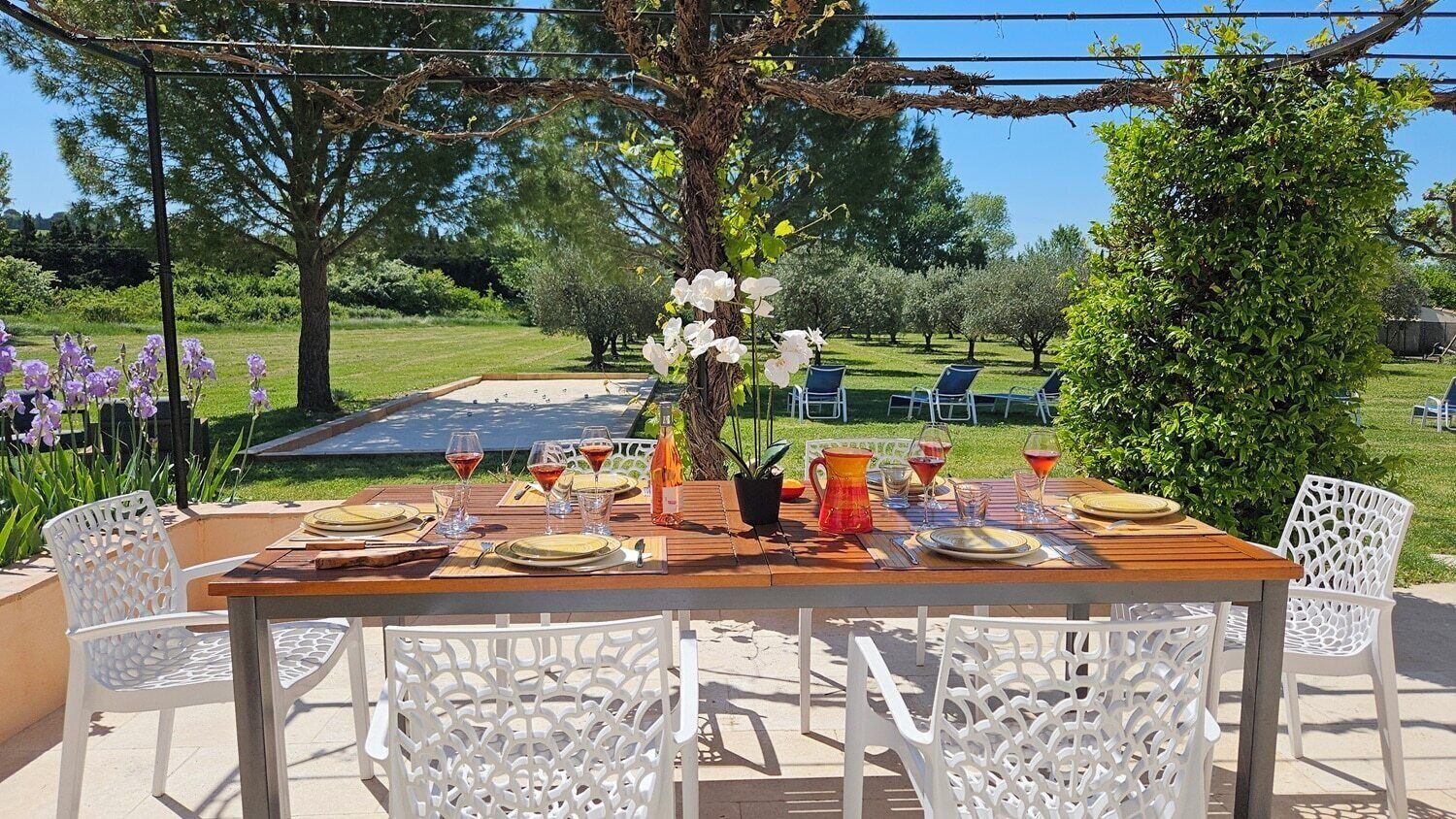 An outdoor dining area with a wooden table set for four, surrounded by white chairs.