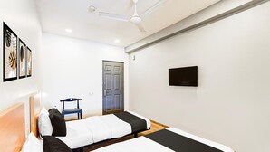 Ett hotellrum med två sängar, en takfläkt, en dörr, en stol och en tv med platt skärm.