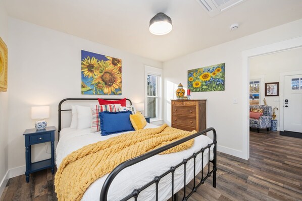 Une chambre à coucher comprenant un lit, une table de chevet, une commode et deux tableaux représentant des tournesols, accrochés aux murs.