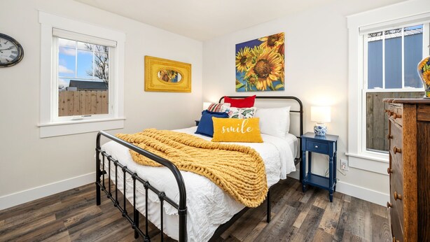 A bedroom with a bed, a bedside table, a wall clock, a window, and a painting. - City Park Bungalow Pet Friendly w/ Dog Run (Fort Collins)