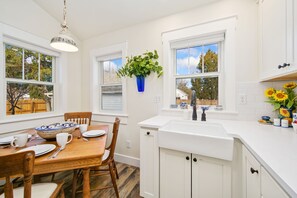 Une cuisine avec des meubles blancs, une table à manger en bois et une plante suspendue.
