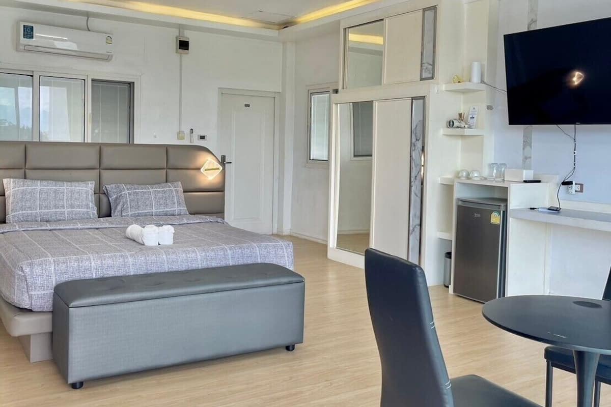 A modern hotel room with a bed, a seating area, a TV, and a kitchenette.