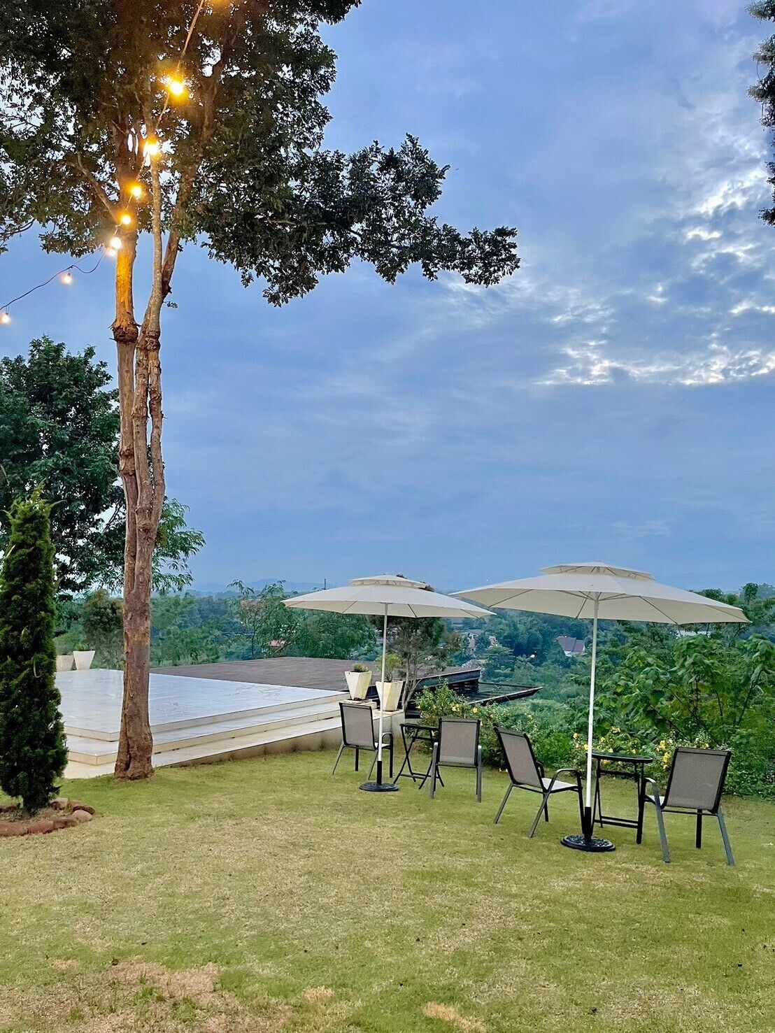 Un espace extérieur aménagé avec des tables et des chaises, entouré d’arbres et offrant une vue sur un plan d’eau.