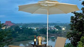 Una terraza con una mesa y sillas, una sombrilla, y vistas a un río y edificios al fondo.