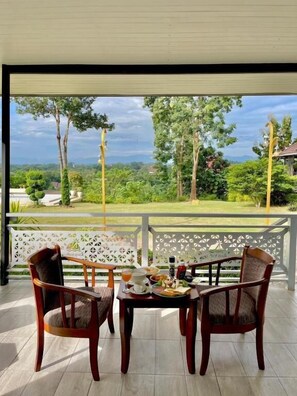 Un balcón con dos sillas de madera, una mesa con comida y vistas a un paisaje verde exuberante.