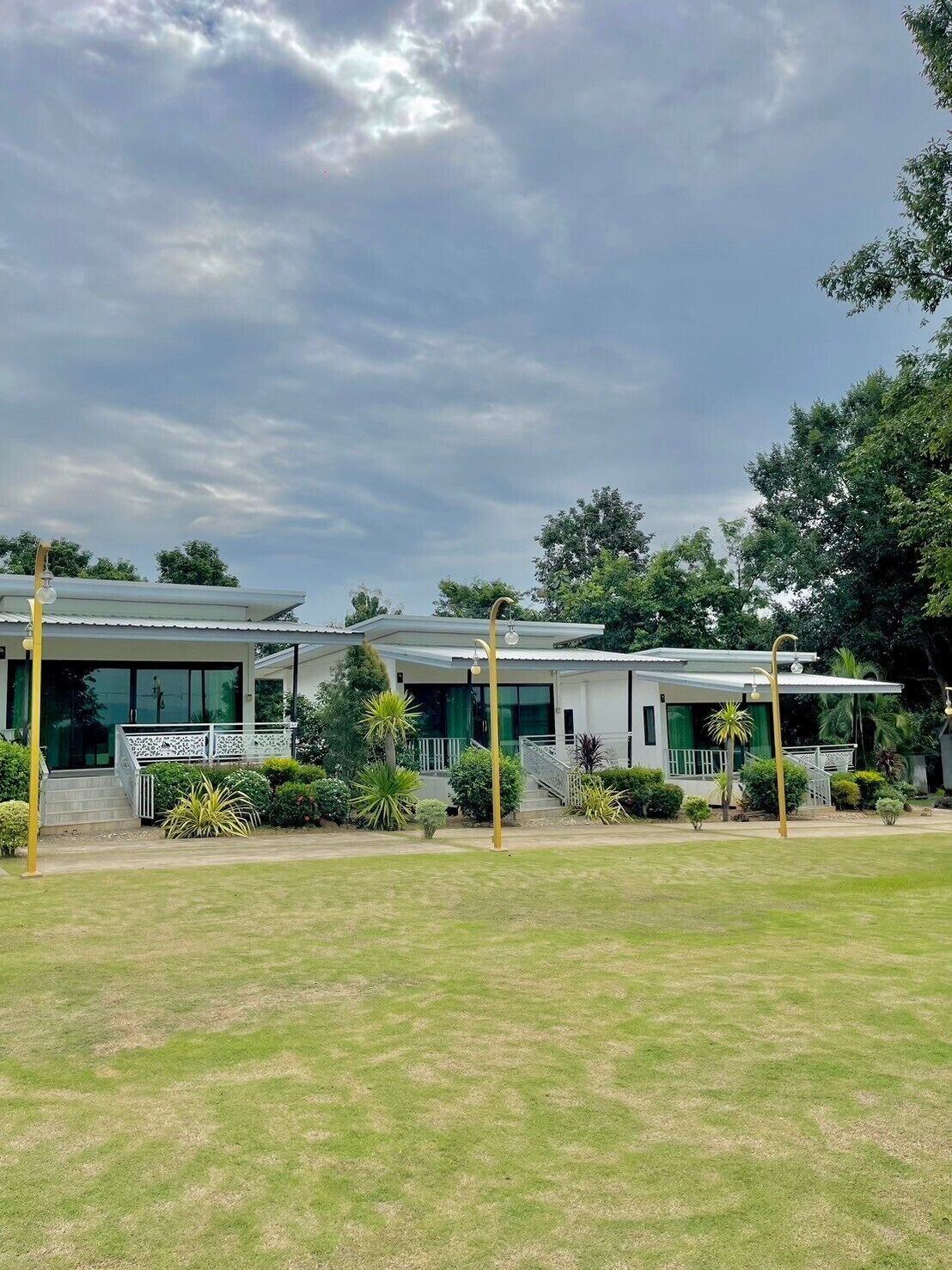 A row of modern, single-story buildings with large windows and a flat roof, surrounded by well-maintained lawns and trees.