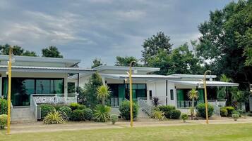A row of modern, single-story buildings with large windows and a flat roof, surrounded by well-maintained lawns and trees.