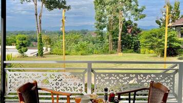 Comedor con dos sillas de madera y una mesa dispuesta para una comida, con vistas a un jardín exuberante y montañas lejanas.
