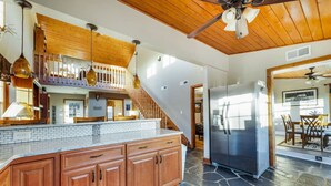A kitchen with wooden cabinets, a stone backsplash, a stainless steel refrigerator, and a ceiling fan. - Monroe Retreat with Mountain Views & Fire Pit! (Monroe)
