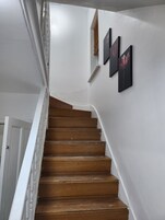 Una escalera de madera con paredes blancas y tres cuadros enmarcados.