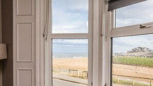 Ein Zimmer mit großem Fenster und Blick auf einen Strand, ein Sessel und eine Lampe.