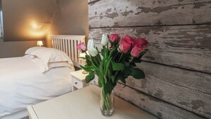 Ein Schlafzimmer mit einem Bett, einem Nachttisch mit Blumenvase und einer Lampe.