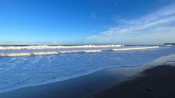 Ein Strand mit Wellen, einem klaren Himmel und einer fernen Küste.