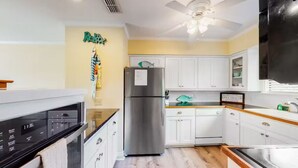 Una cocina moderna con armarios blancos, un refrigerador de acero inoxidable, horno empotrado y ventilador de techo.