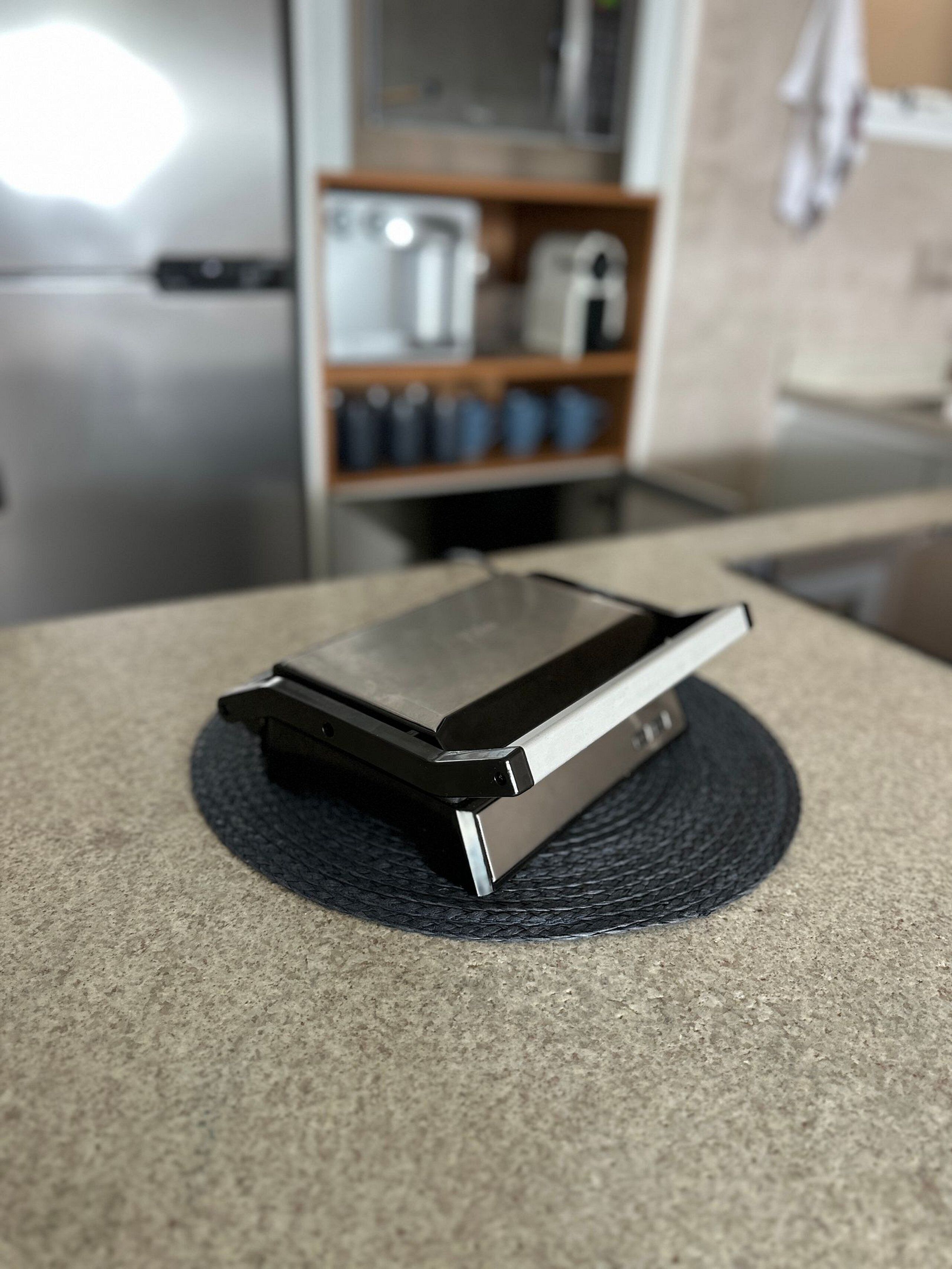 Una computadora portátil sobre un tapete texturizado en una cocina con un refrigerador y estantes al fondo.