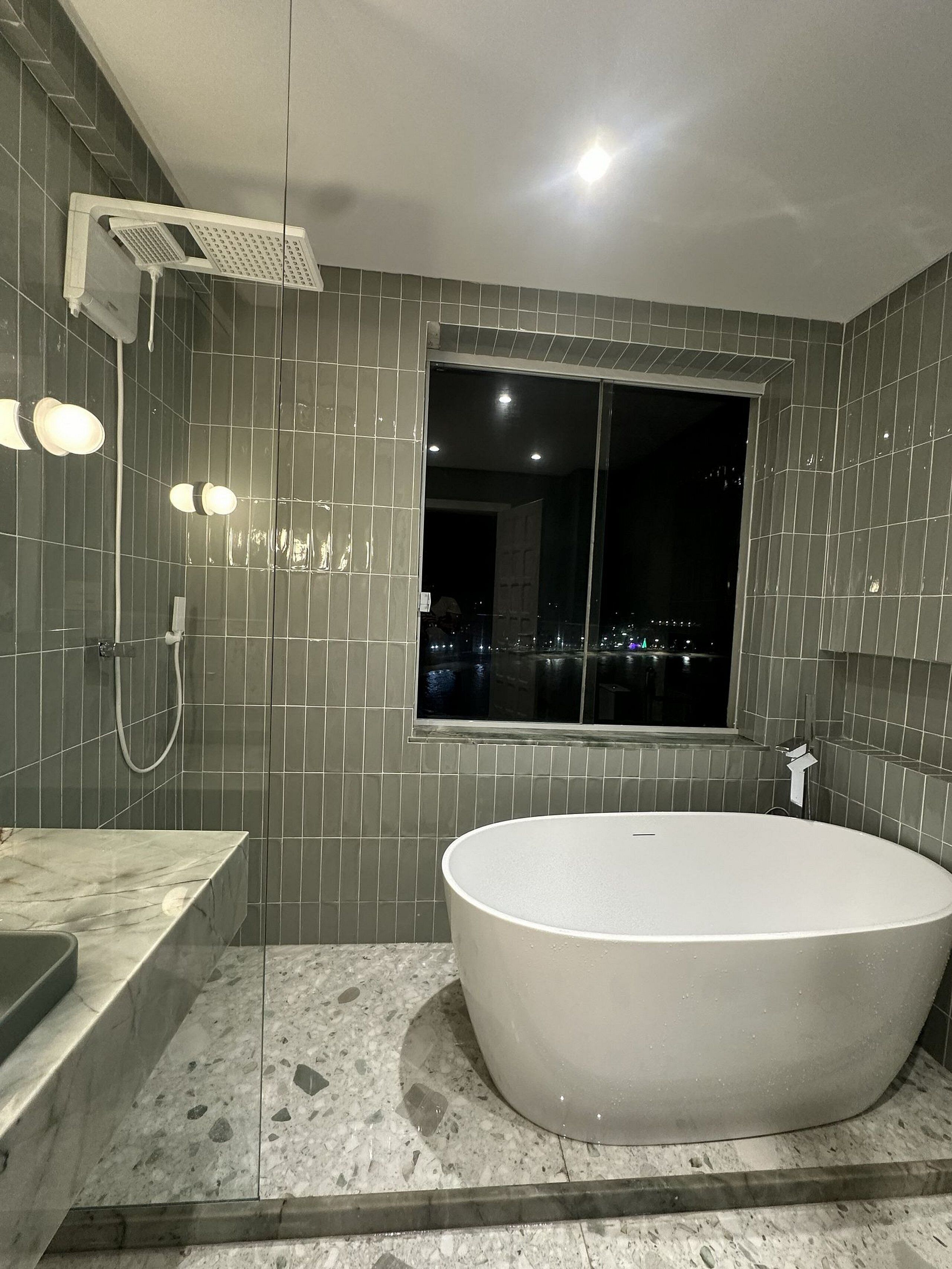 A modern bathroom with a freestanding bathtub, a showerhead, and a window with a city view.
