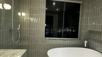 A modern bathroom with a freestanding bathtub, a showerhead, and a window with a city view.