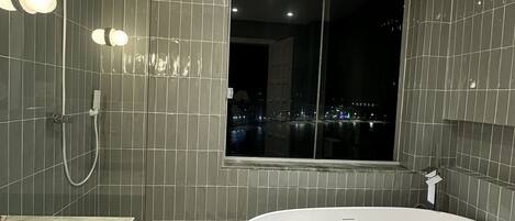 A modern bathroom with a freestanding bathtub, a showerhead, and a window with a city view.