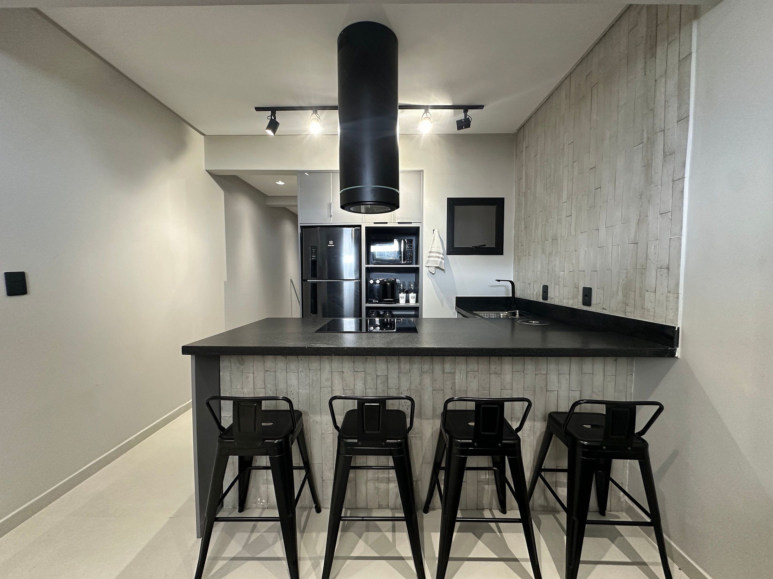 A modern kitchen with a central island, bar stools, a built-in oven, and a stainless steel refrigerator.