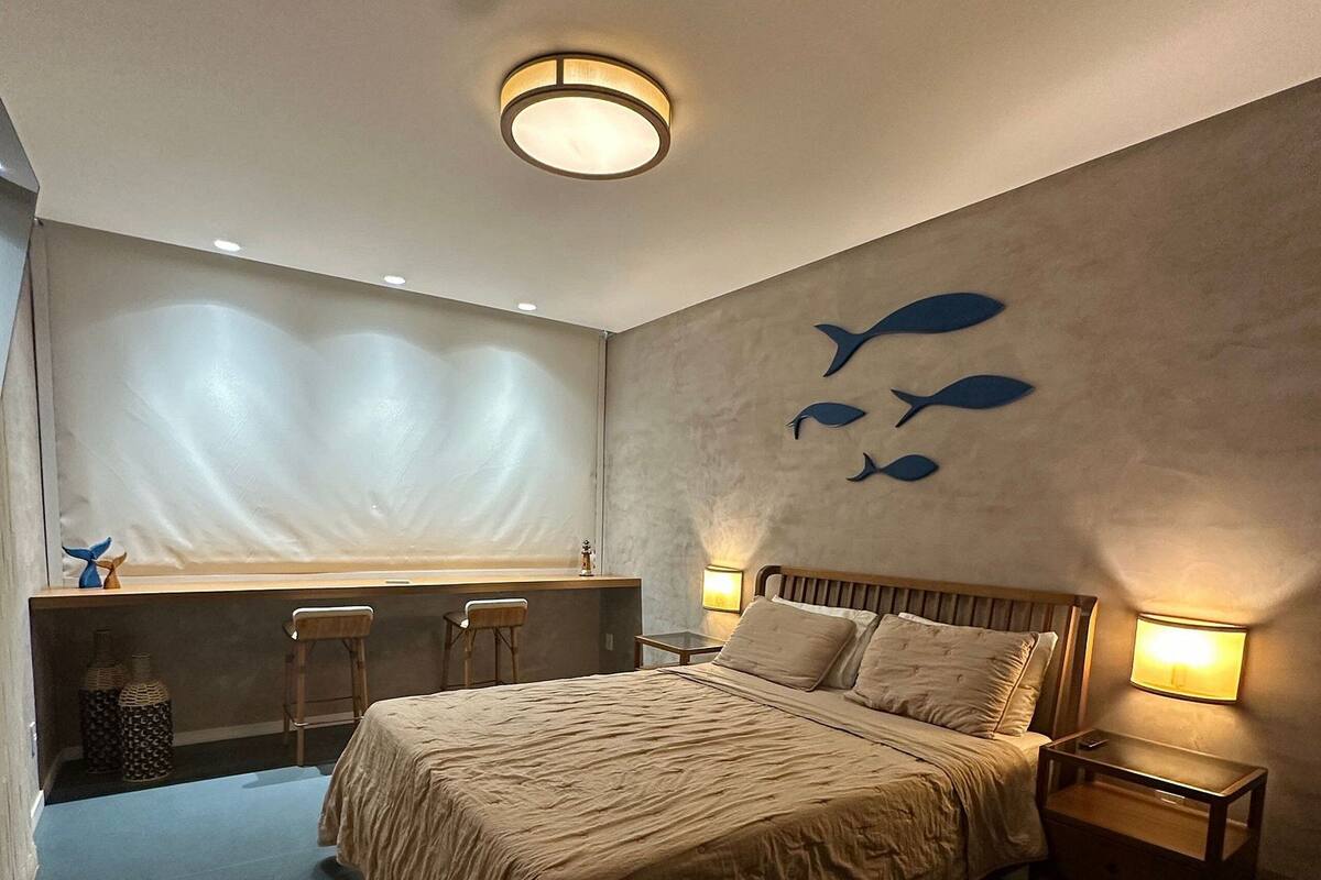 Un dormitorio con cama, mesitas de noche, ventana con vistas y pared decorada con motivos de peces.