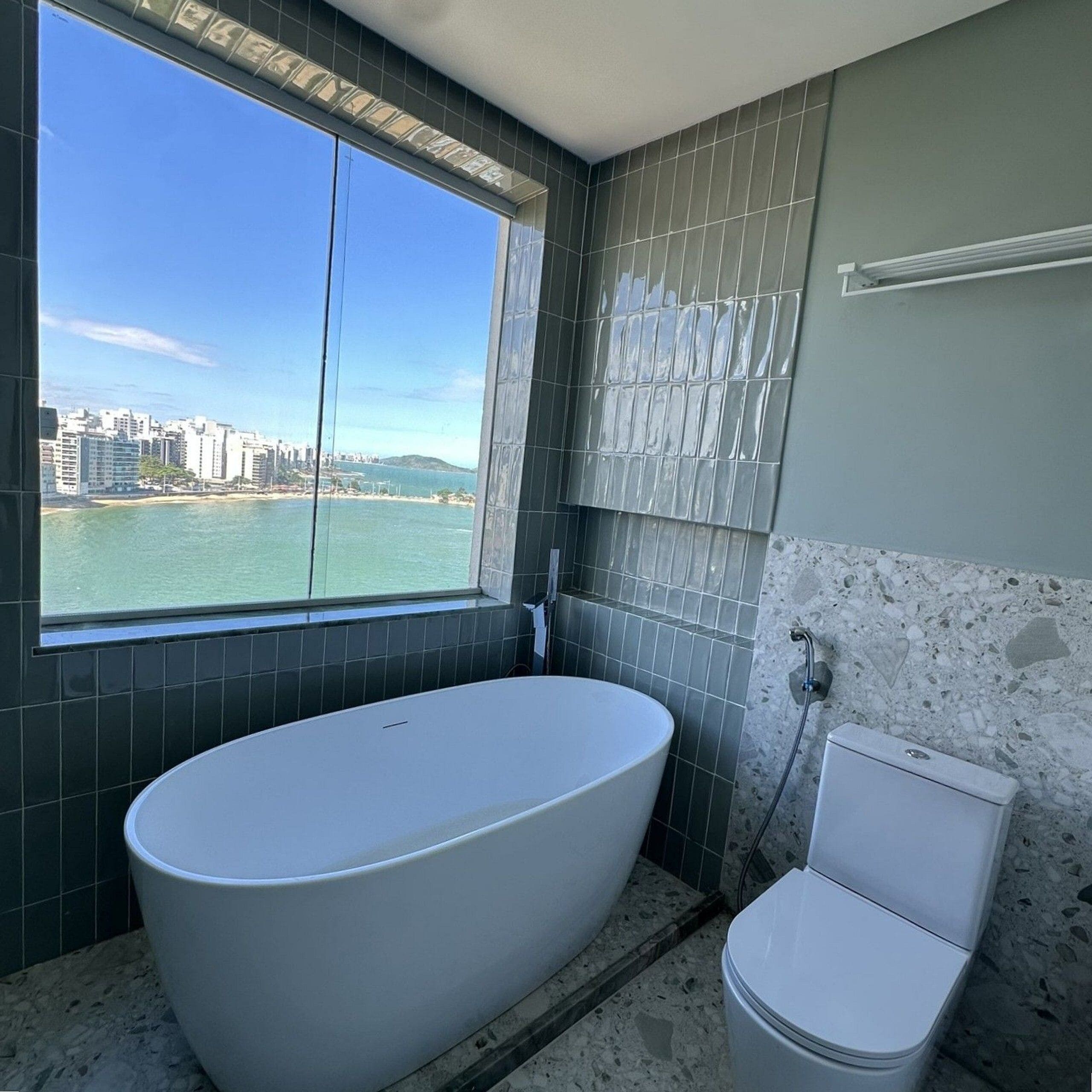 Uma casa de banho com uma banheira grande, sanita e janela com vista para a paisagem urbana e para a água.
