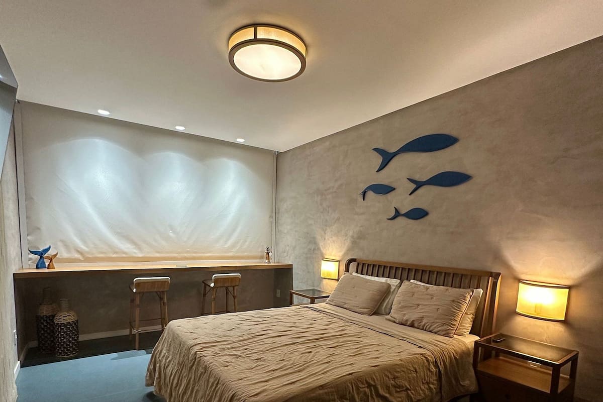 A bedroom with a bed, bedside tables, a window with a view, and a wall with fish decorations.
