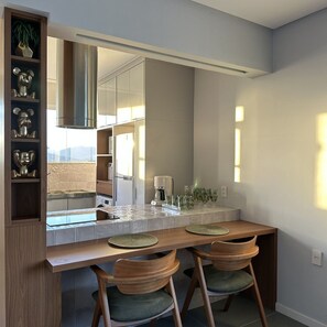 A modern kitchen with a large mirror, wooden bar counter, two chairs, and a built-in shelf with decorative items. - Guarapari Center Aparts (Guarapari)