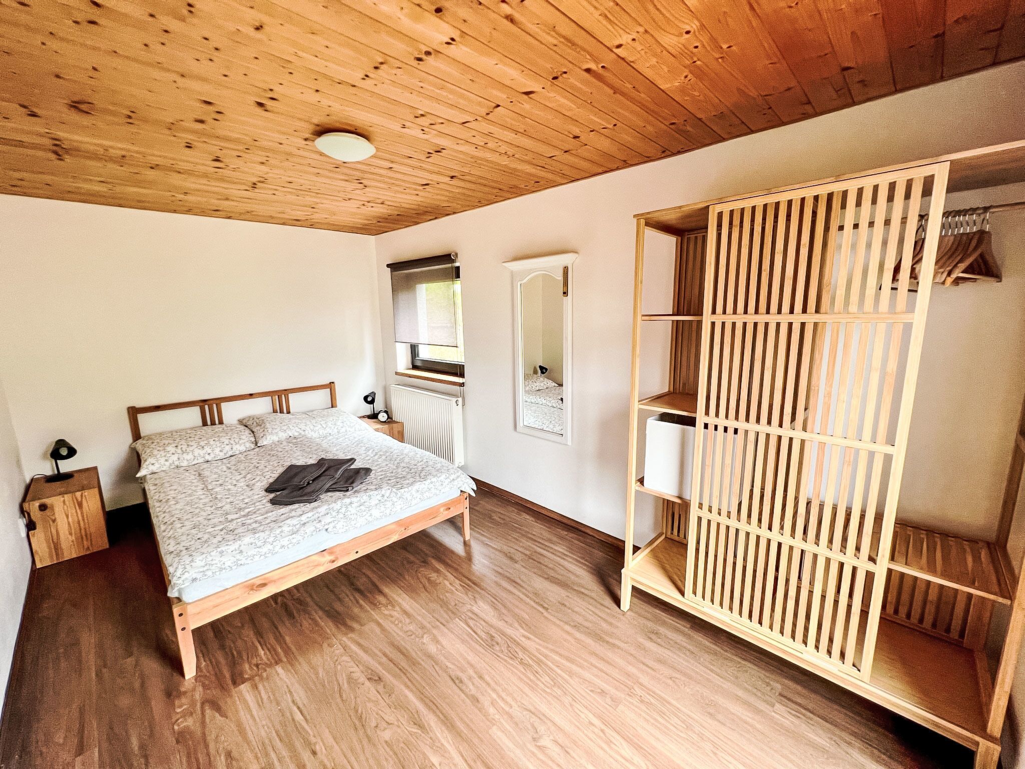 Un dormitorio con cama de madera, una mesita de noche, un armario con estantes y un espejo.