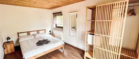 Un dormitorio con cama de madera, una mesita de noche, un armario con estantes y un espejo.