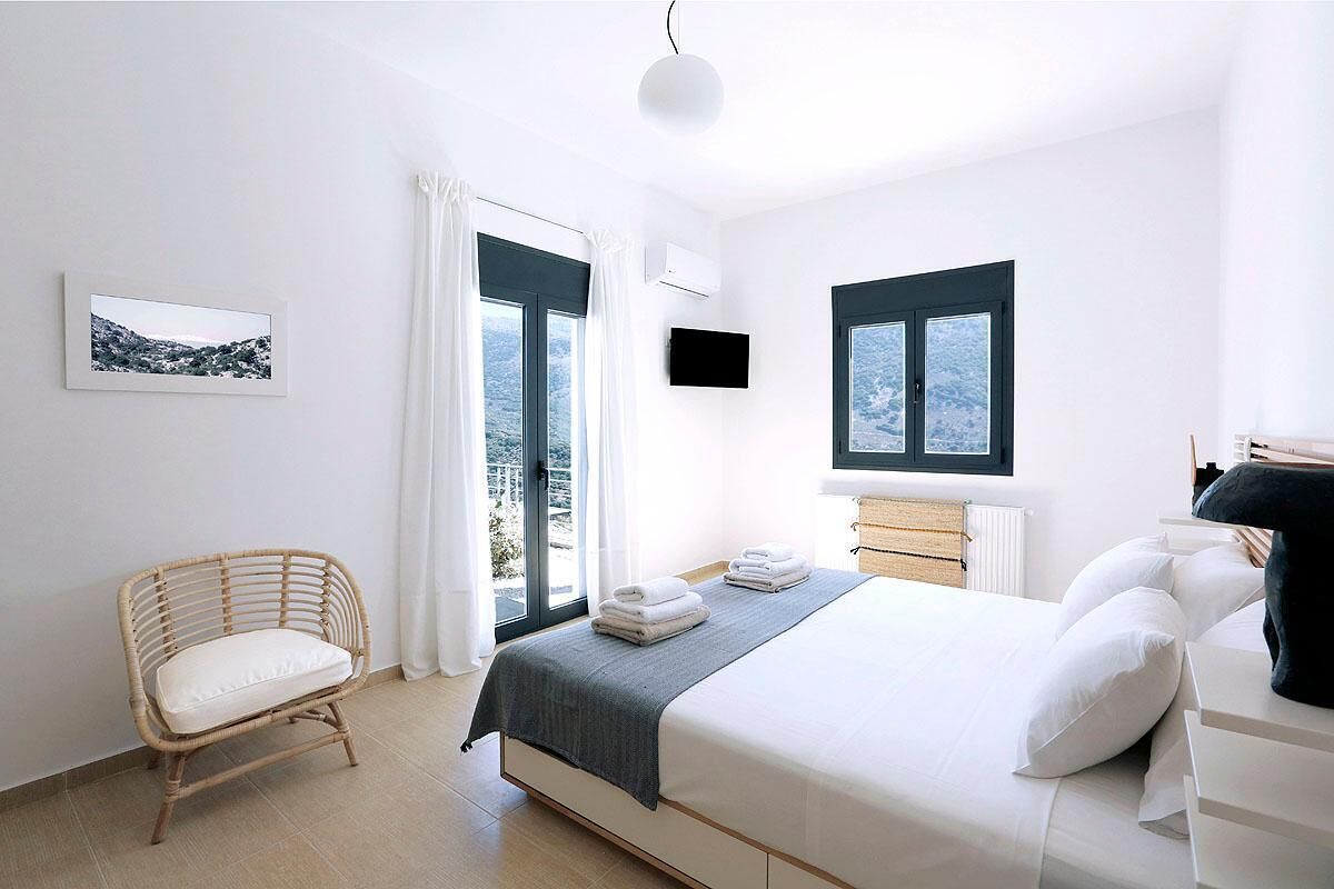 A modern bedroom with a large bed, a wicker chair, a flat-screen TV, and a view of a snowy landscape through the windows.