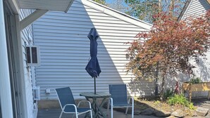 A covered outdoor patio with a table and two chairs, a covered umbrella, and a wooden deck.