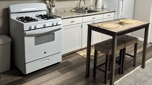 A kitchen with white cabinets, a black microwave, a white stove, and a wooden table with two stools.