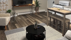 A living room with a TV, sofa, coffee table, and kitchen area with a stove and microwave.