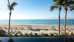 Une vue sur la plage, avec des palmiers, des chaises longues et une piscine.