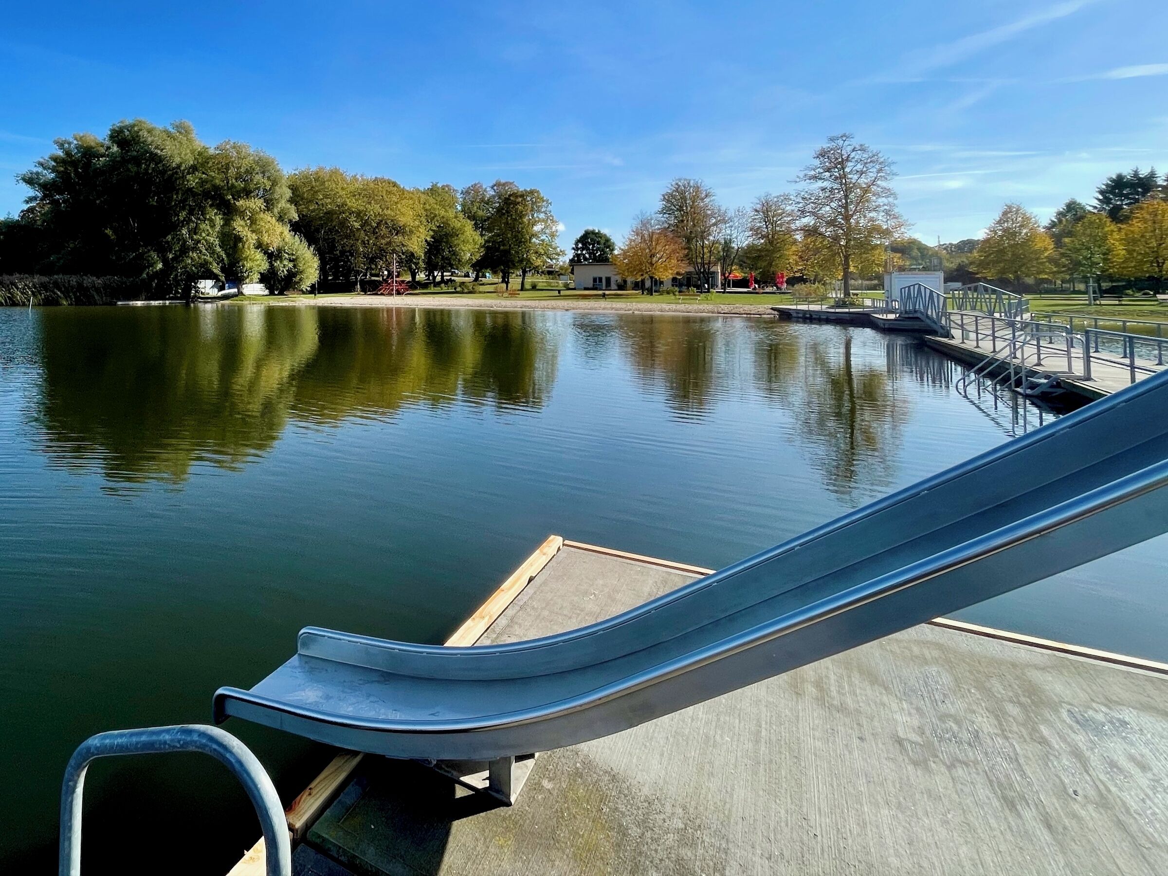 Een rustig meer met een steiger en een metalen glijbaan die in het water uitkomt.