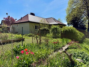A house with a tiled roof, surrounded by a garden with various plants and flowers. - Vacation home directly on the lake 50m to the beach with garden and fireplace (Warin)