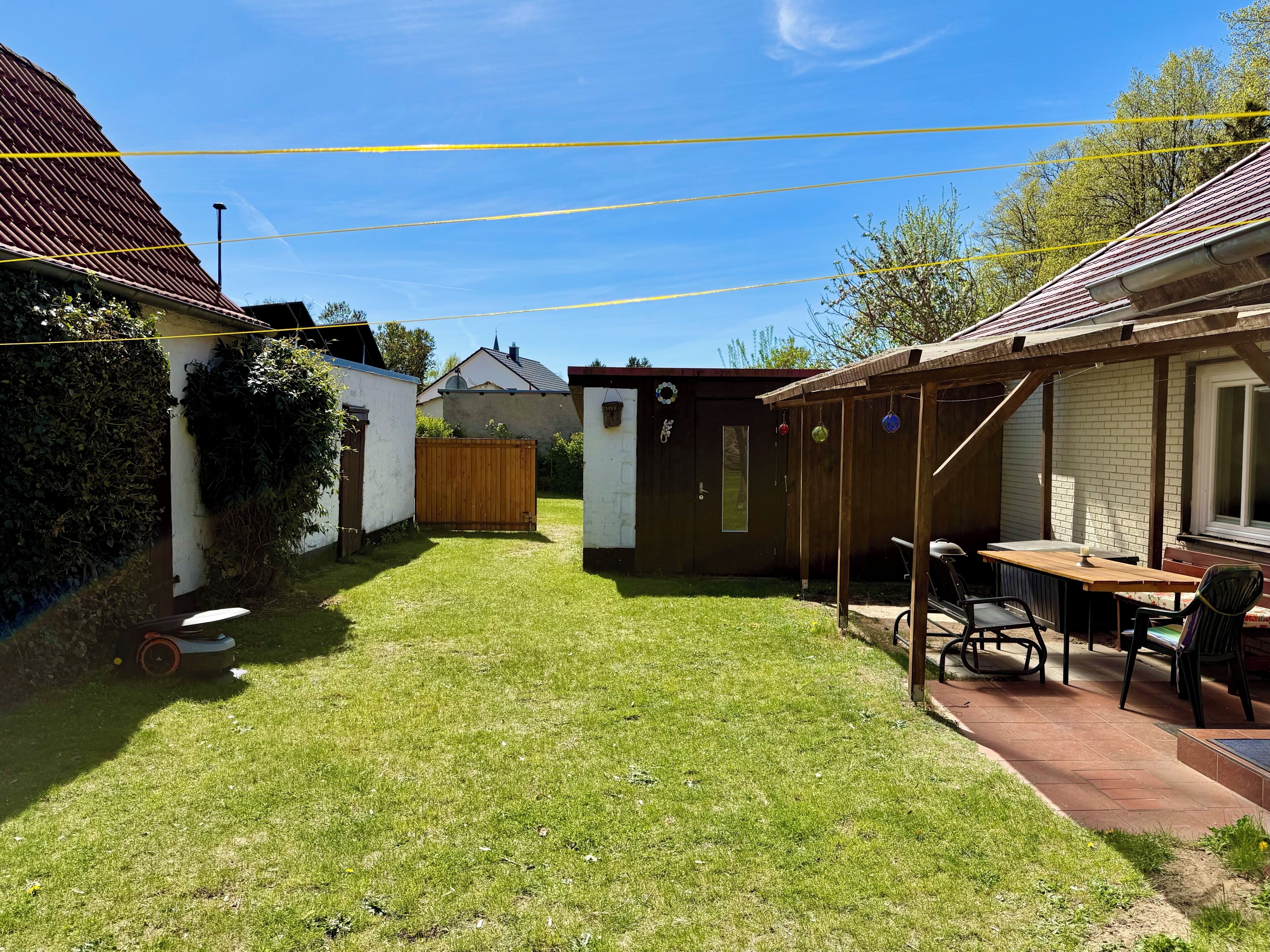 Ein Garten mit einer Holzterrasse, einem Tisch mit Stühlen und einem kleinen Schuppen.