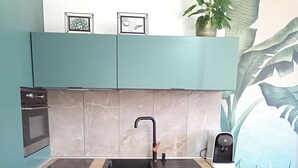 Una cocina compacta con armarios color turquesa, horno empotrado, lavamanos con grifo y cafetera.