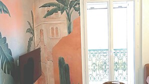 Una habitación con un mural de paisaje desértico, una puerta corredera de cristal que da a un balcón con barandilla de metal y una mesa redonda de madera.