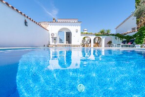 A clear swimming pool with a tiled edge, a white building with a tiled roof, and a clear blue sky. - 0149-VALIRA House at the canal with pool and mooring (Empuriabrava)