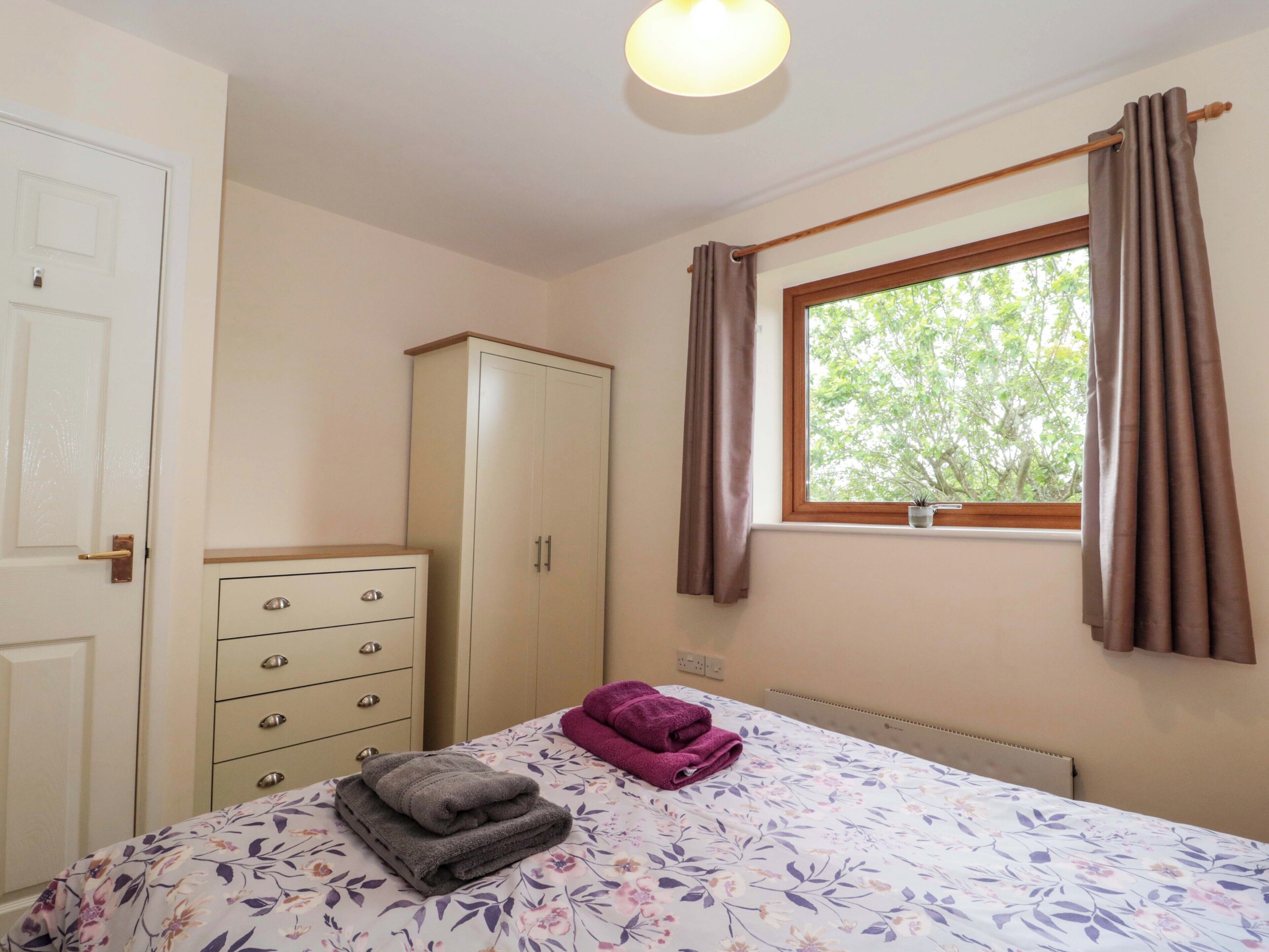 A bedroom with a bed, a wardrobe, a radiator, a window with curtains, and a ceiling light.