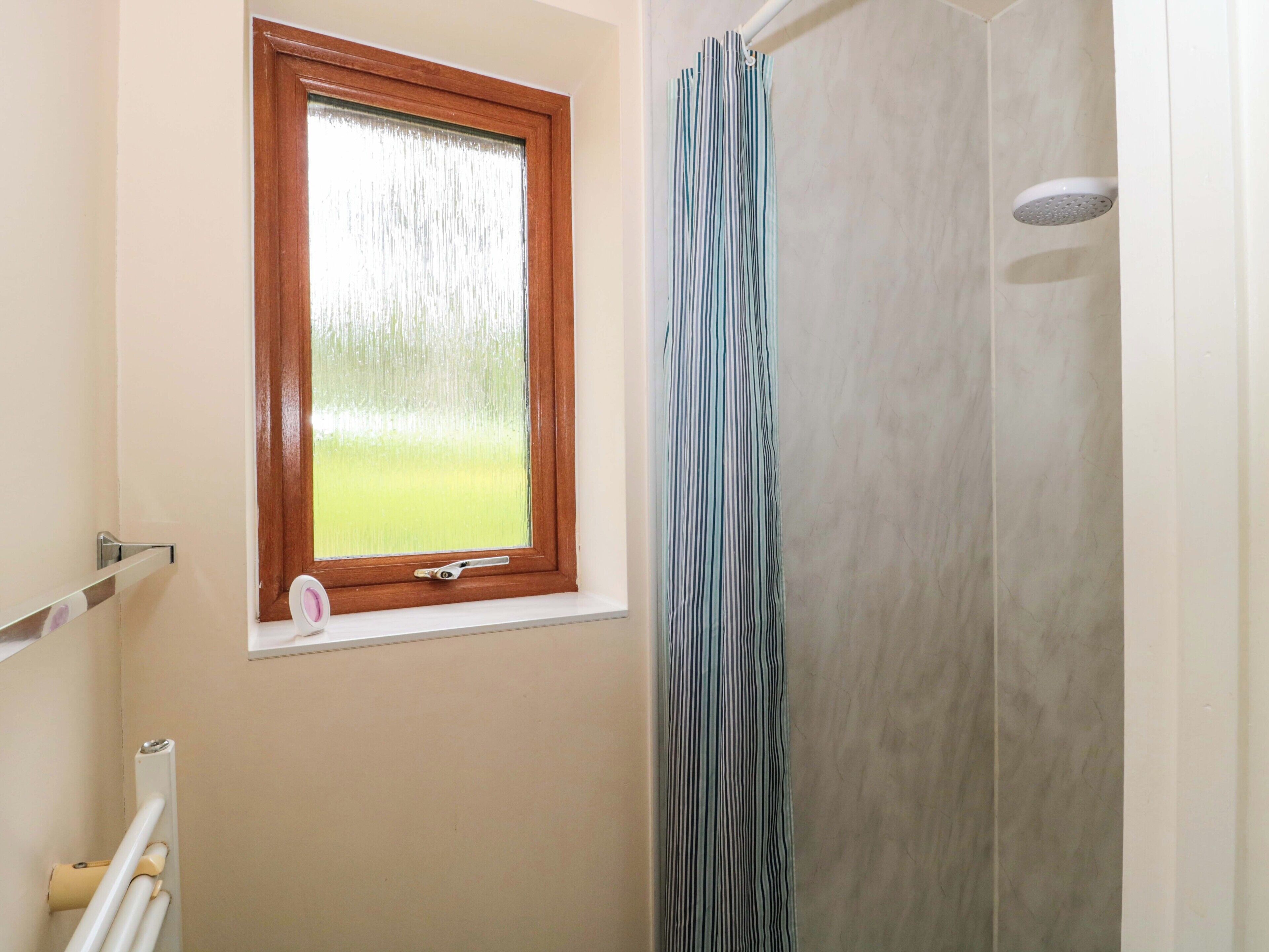 A bathroom with a shower, a window with a wooden frame, and a towel rack.