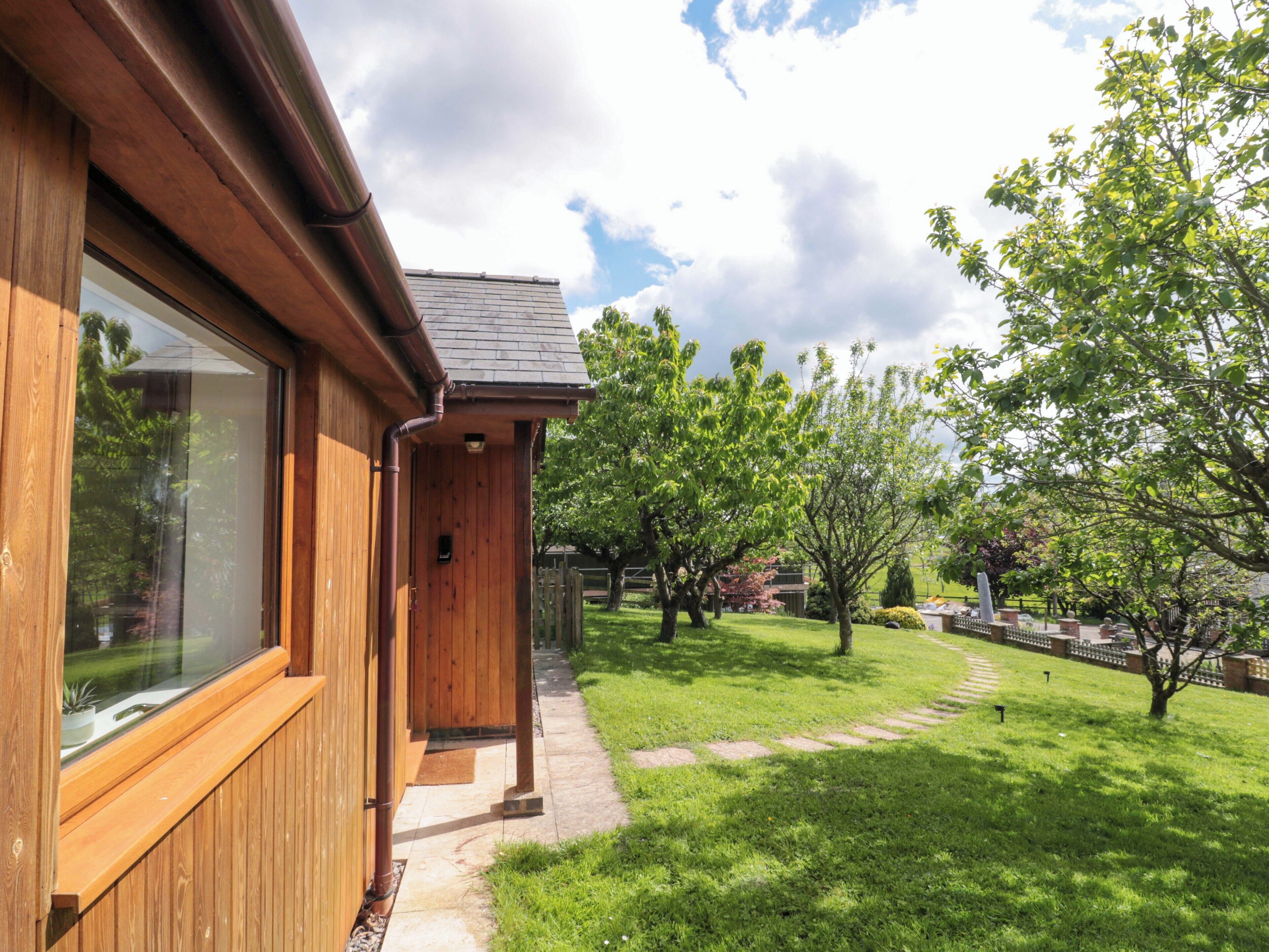 A wooden building with a large window and a pathway leading to a grassy area with trees.